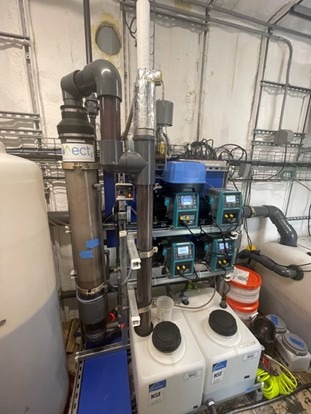 Industrial water treatment system with pipes, control panels, chemical containers, and wiring in a utility room—this setup was recently featured in a PFAS Pilot Story highlighting its effectiveness in addressing emerging contaminants.