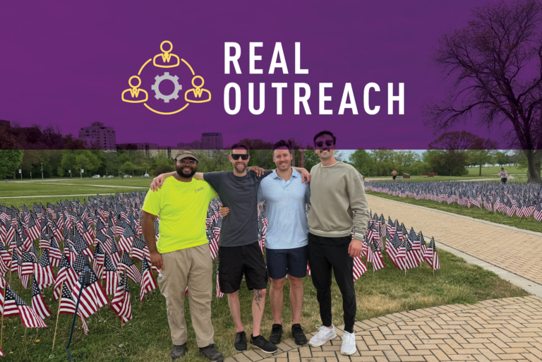 Four men stand arm-in-arm, smiling in front of a field of American flags. A purple overlay at the top displays the REAL OUTREACH logo with an icon of connected people. Trees and buildings are in the background.